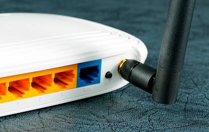Traseira de um equipamento de rede branco, com quatro portas LAN amarelas, uma porta azul e uma antena preta